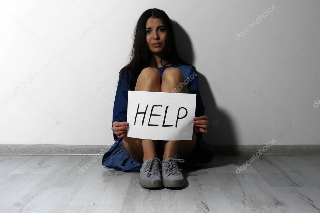 Abused young woman with sign HELP near white wall. Domestic viol