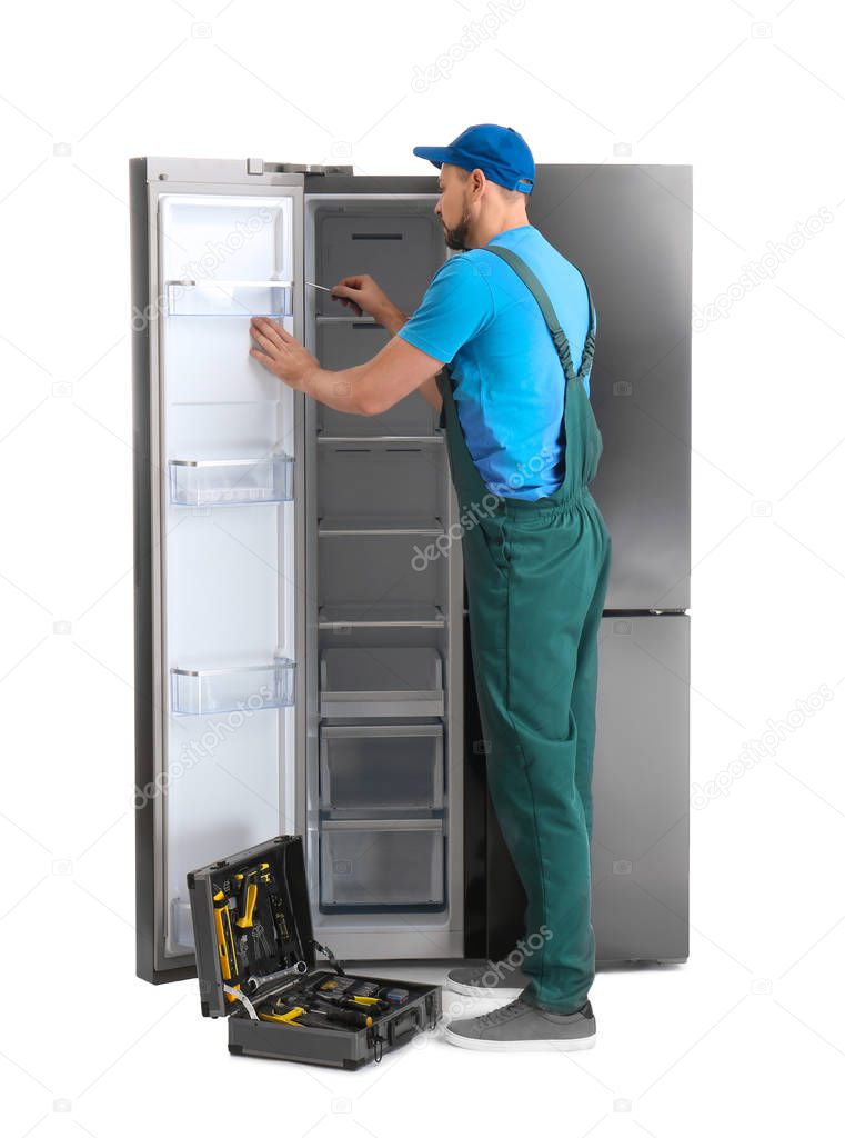 Male technician repairing refrigerator on white background