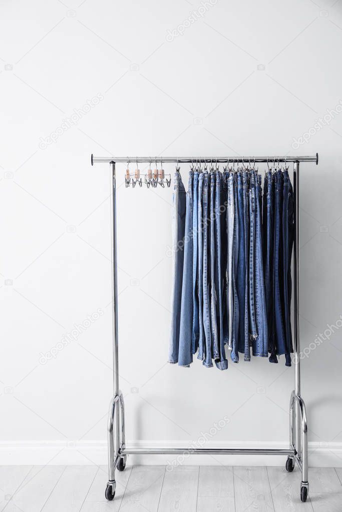 Rack with different jeans near white wall