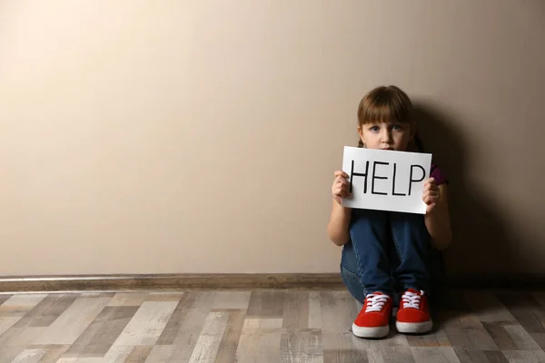 Грустная маленькая девочка с табличкой HELP, сидящая на полу в помещении, пространство f — стоковое фото