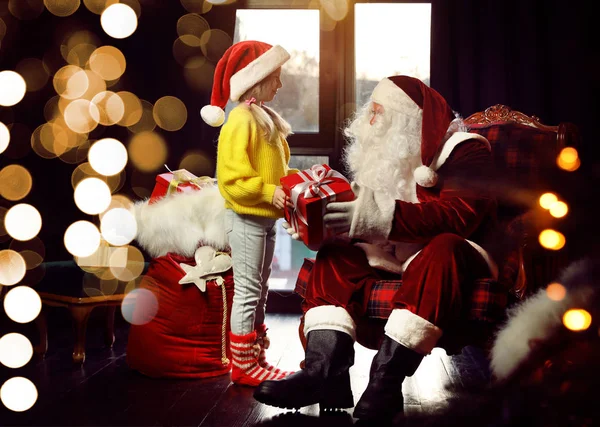 Santa Claus giving Christmas gift to little girl near window ind — Stock Photo, Image