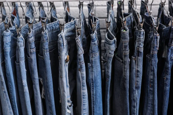Rack met stijlvolle jeans in de buurt van bakstenen muur, close-up — Stockfoto