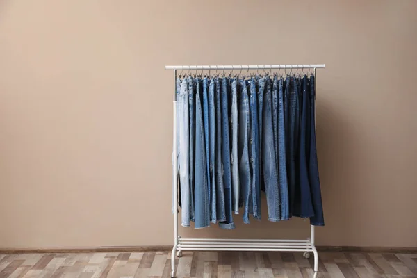 Rack with stylish jeans on near beige wall — Stok Foto
