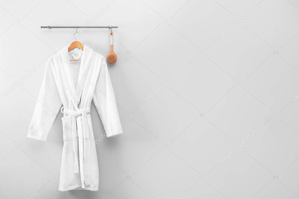 Hanger with clean bathrobe and brush on light wall. Space for text