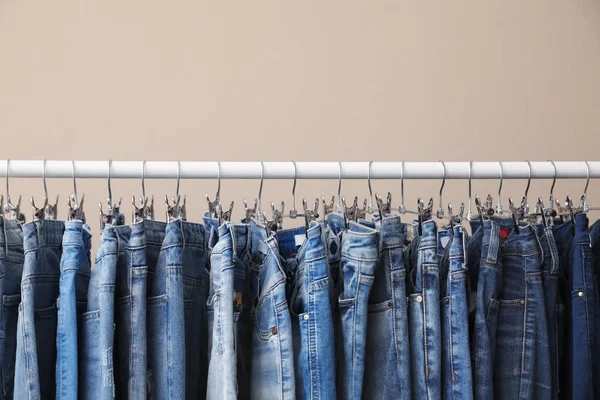 Rack with stylish jeans on beige background, closeup — Stock Photo, Image