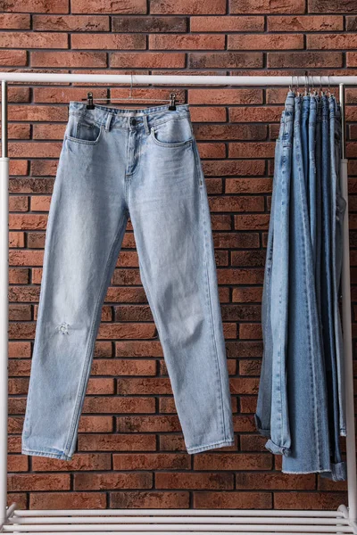 Стелаж зі стильними джинсами біля цегляної стіни — стокове фото