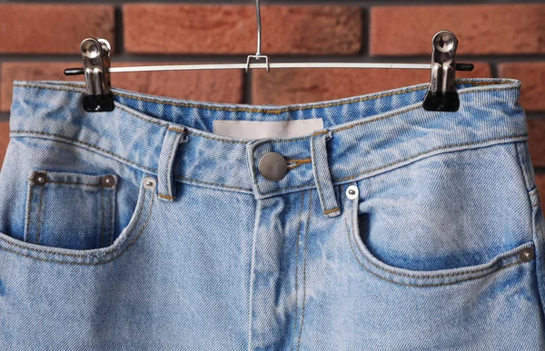 Appendiabiti con jeans alla moda vicino al muro di mattoni, primo piano — Foto Stock