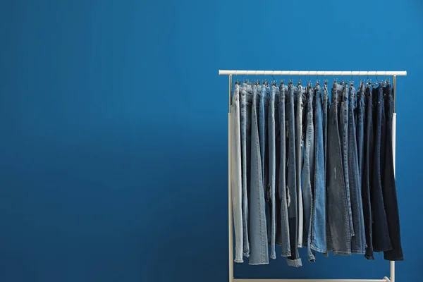 Rack with stylish jeans on blue background. Space for text — ストック写真