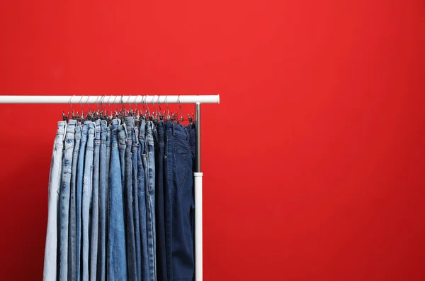 Rack with stylish jeans on red background. Space for text — ストック写真