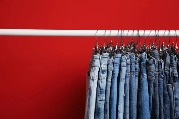 Rack with stylish jeans on red background — 스톡 사진