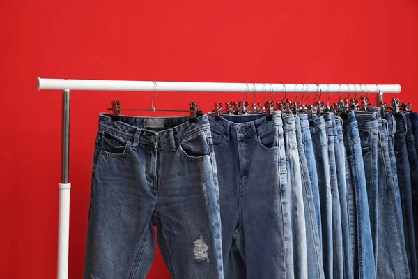 Cremalheira com jeans elegantes no fundo vermelho, close-up — Fotografia de Stock