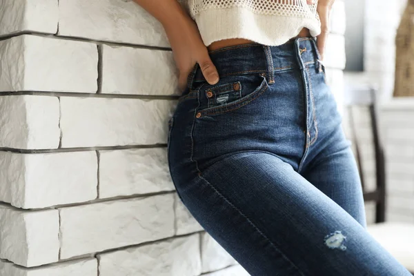 Mulher vestindo jeans perto da parede de tijolo dentro de casa, close-up — Fotografia de Stock