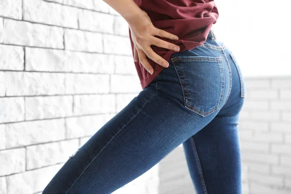 Mulher vestindo jeans perto da parede de tijolo dentro de casa, close-up — Fotografia de Stock