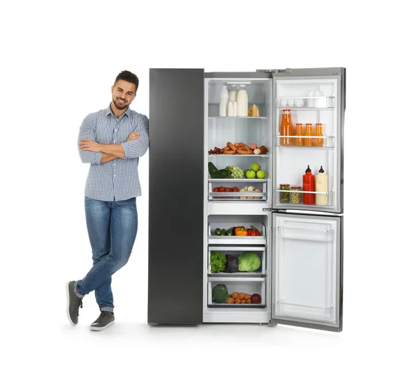 Молодой человек возле открытого холодильника на белом фоне — стоковое фото
