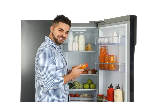 Молодой человек берет сок из холодильника на белом фоне — стоковое фото