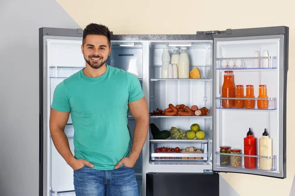 Feliz joven cerca de refrigerador abierto en el interior — Foto de Stock