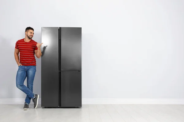 Счастливый молодой человек возле холодильника в помещении, пространство для текста — стоковое фото