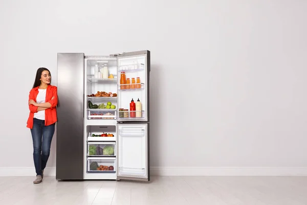 Šťastná mladá žena v blízkosti otevřené ledničky uvnitř, prostor pro text — Stock fotografie