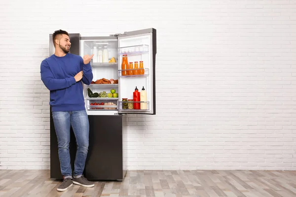 Feliz joven cerca de refrigerador abierto en el interior, espacio para el texto — Foto de Stock