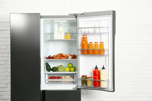 Открытый холодильник с едой возле стены из белого кирпича — стоковое фото