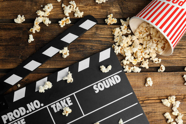 Tasty fresh pop corn and clapboard on wooden table, flat lay