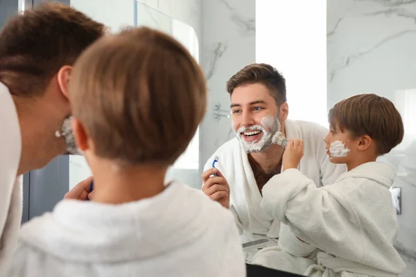 Dad and son with shaving foam on their faces having fun in bathr