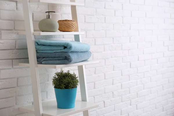 Clean soft towels and soap dispenser on shelves near white brick wall. Space for text