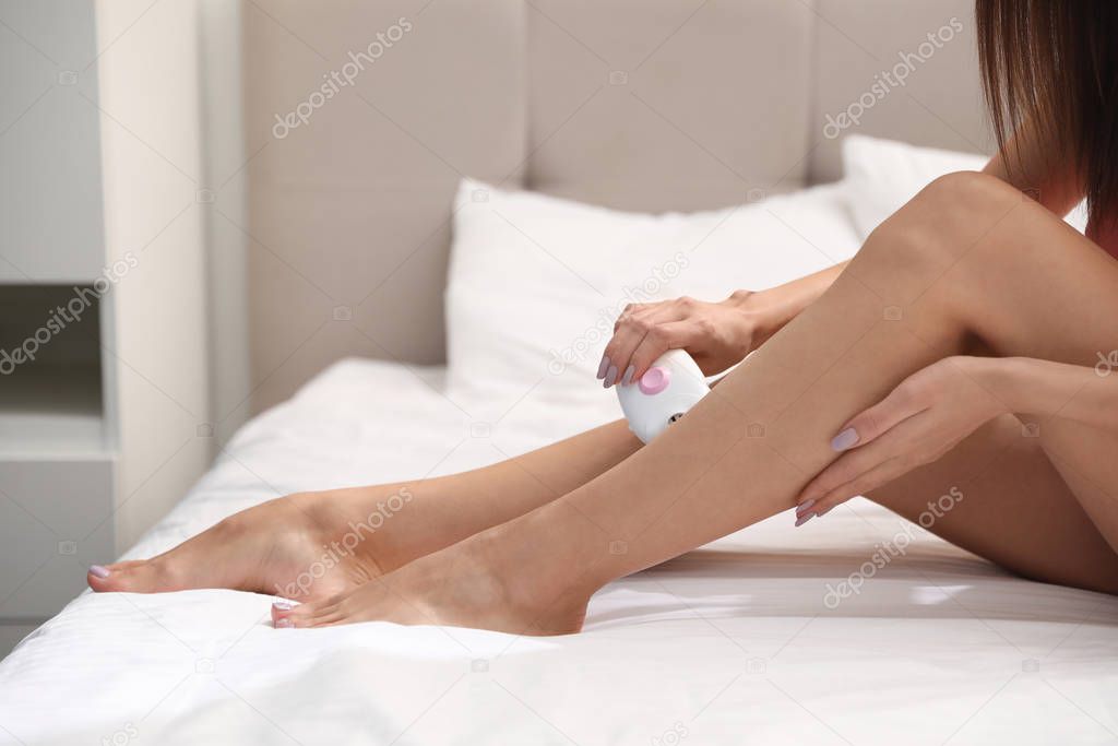 Young woman epilating her legs in bedroom, closeup