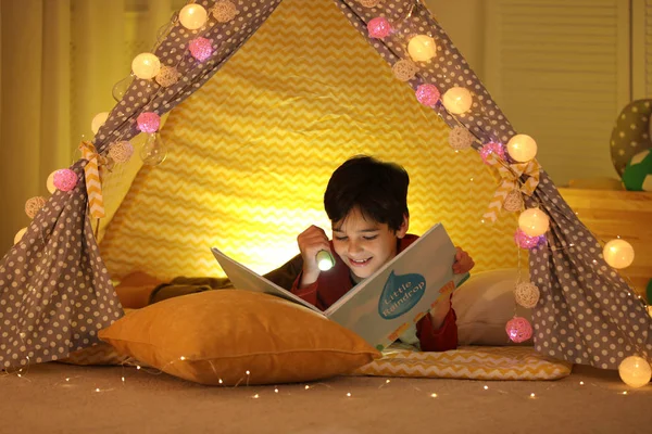 Chlapec s baterkou čtení knihy ve stanu doma — Stock fotografie
