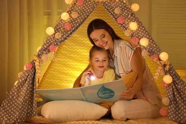 Mãe e filha com lanterna leitura livro em jogar tenda em — Fotografia de Stock