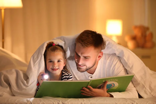 Otec a dcera s baterkou čtení knihy pod dekou — Stock fotografie