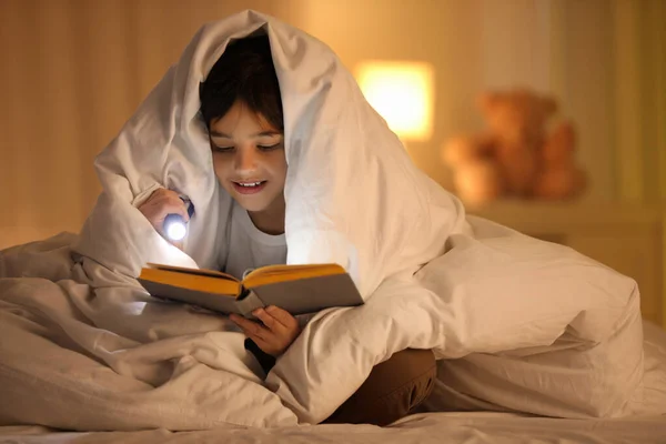 家里拿着手电筒看书的男孩 — 图库照片