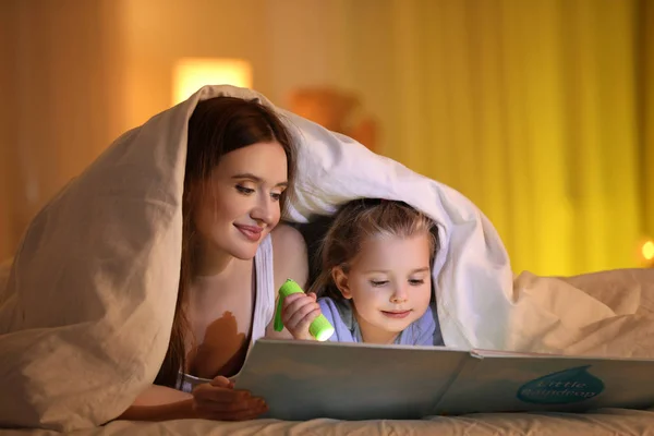 Mãe e filha com lanterna livro de leitura sob cobertor um — Fotografia de Stock