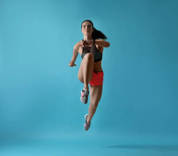 Atletica giovane donna in esecuzione su sfondo azzurro — Foto Stock
