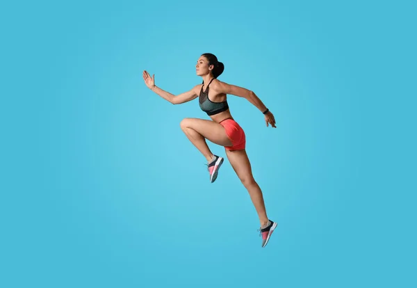 Mujer joven atlética corriendo sobre fondo azul claro, vista lateral —  Fotos de Stock