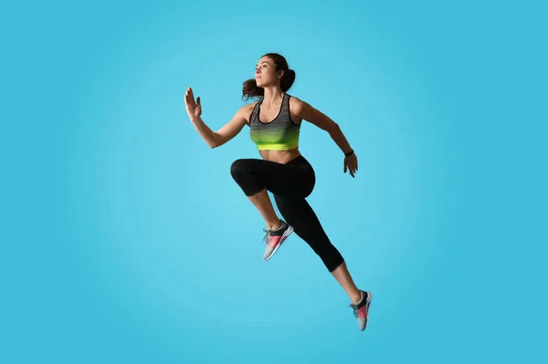 Sportowa młoda kobieta biegnie na jasnoniebieskim tle, widok z boku — Zdjęcie stockowe