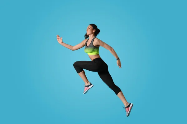 Atletisk ung kvinna kör på ljusblå bakgrund, sidovy — Stockfoto