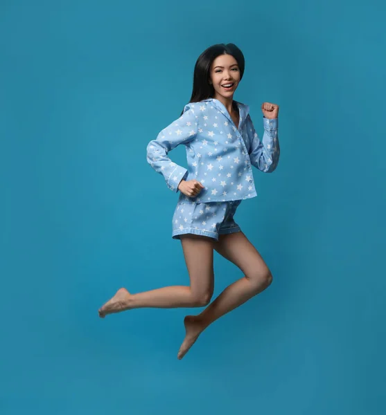 Beautiful Asian woman in pajamas jumping on blue background. Bed