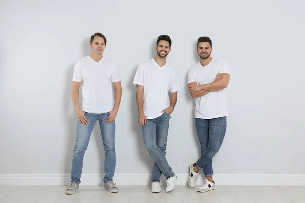 Grupo de hombres jóvenes en jeans con estilo cerca de la pared de luz — Foto de Stock