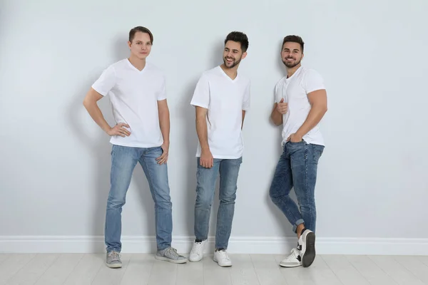 Skupina mladých mužů ve stylových džínách u světlé stěny — Stock fotografie