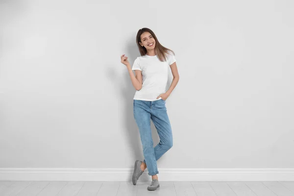 Молодая женщина в стильных джинсах возле светлой стены — стоковое фото