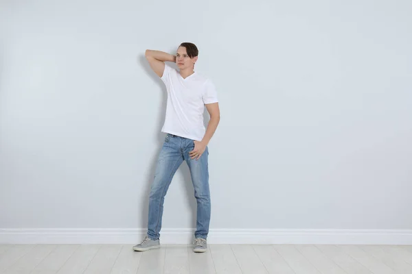 Jovem em jeans elegantes perto da parede leve — Fotografia de Stock