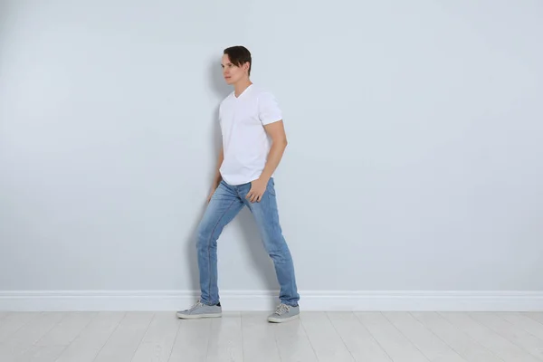 Jovem em jeans elegantes perto da parede leve — Fotografia de Stock