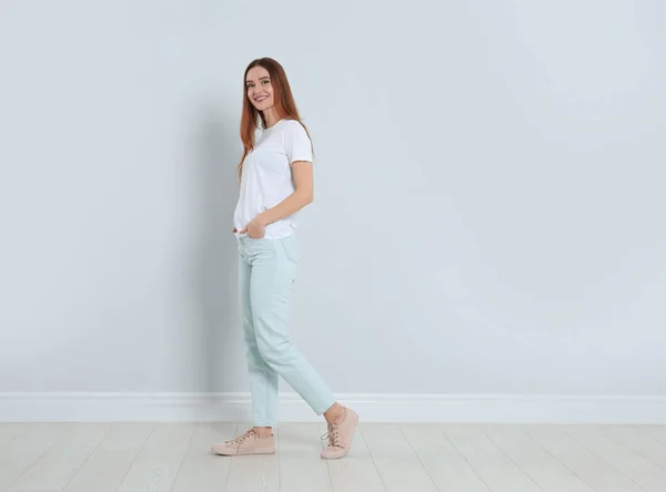 Young woman in stylish jeans near light wall. Space for text — 스톡 사진