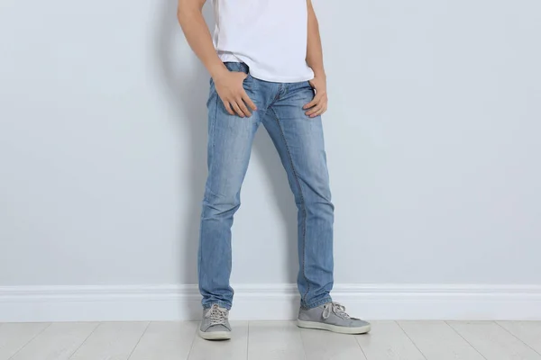Young man in stylish jeans near light wall, closeup — Stock Photo, Image