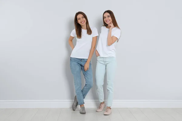 Mujeres jóvenes en jeans elegantes cerca de la pared de luz —  Fotos de Stock