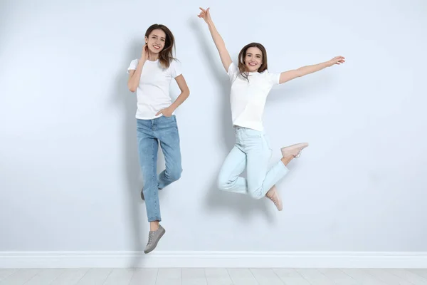 Mujeres jóvenes en jeans elegantes saltando cerca de la pared de luz — Foto de Stock