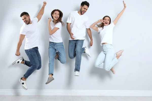 Gruppo di giovani in jeans alla moda che saltano vicino alla parete luminosa — Foto Stock