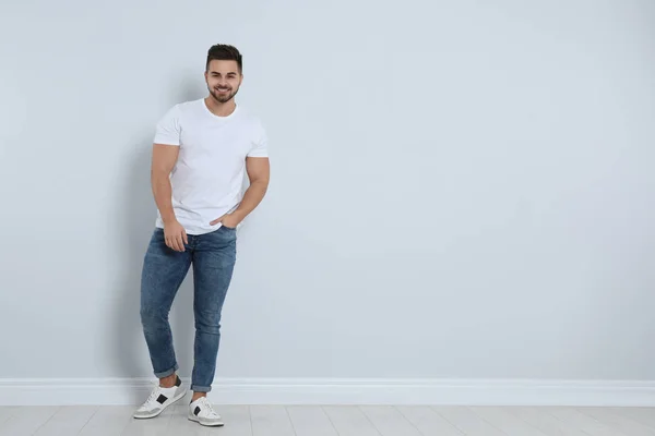 Junger Mann in stylischen Jeans in der Nähe einer Lichtwand. Raum für Text — Stockfoto