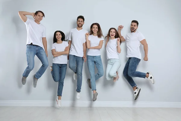 Group of young people in stylish jeans jumping near light wall — Stock Photo, Image